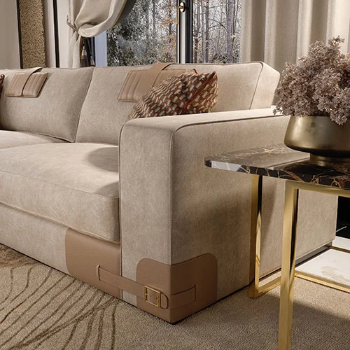 A close view of a beige velvet sofa armrest with leather inserts. Next to a lamp table with gold plated metal base and portoro marble top