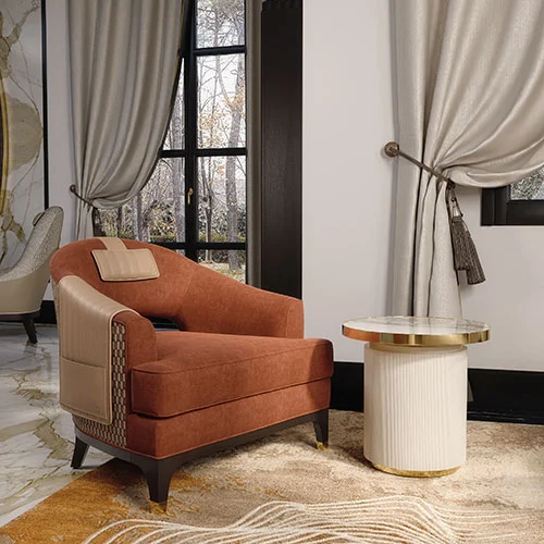 A luxury contemporary armchair in terracotta velvet, with leather headrest, gold plated metal cups, and back ornamental gold plated handle