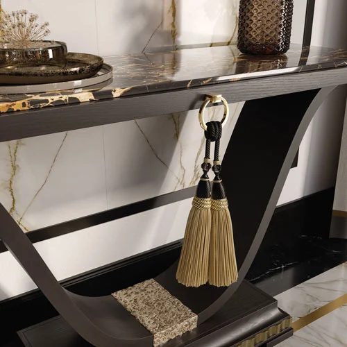 A luxury contemporary black lacquered console, with antique gold leaf accents, decorative fabric tassels and portoro marble top.